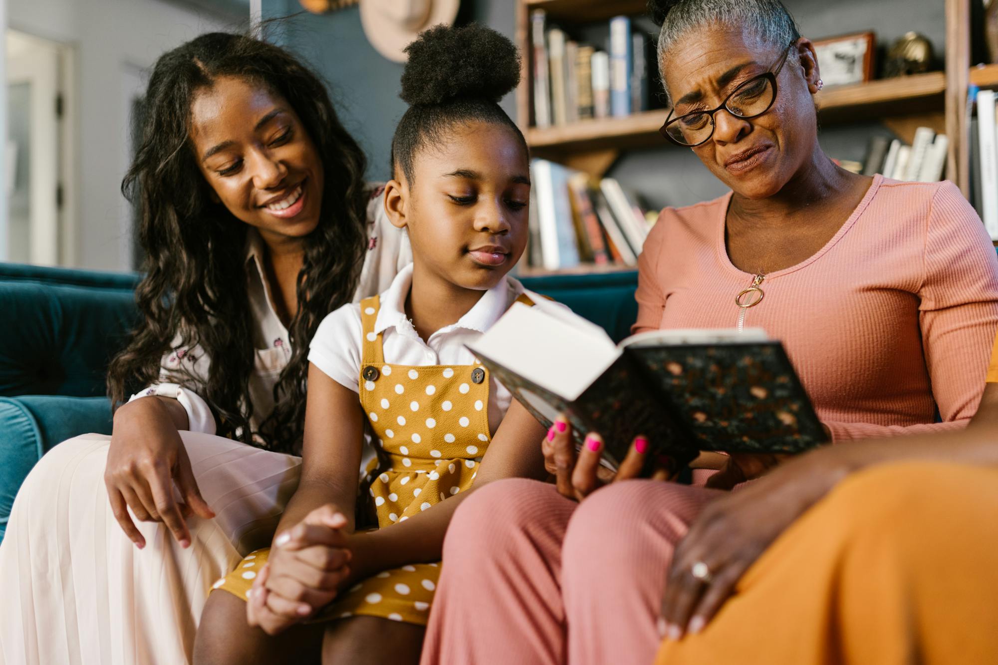 Three generations of a family sitting together on a couch, looking at a book